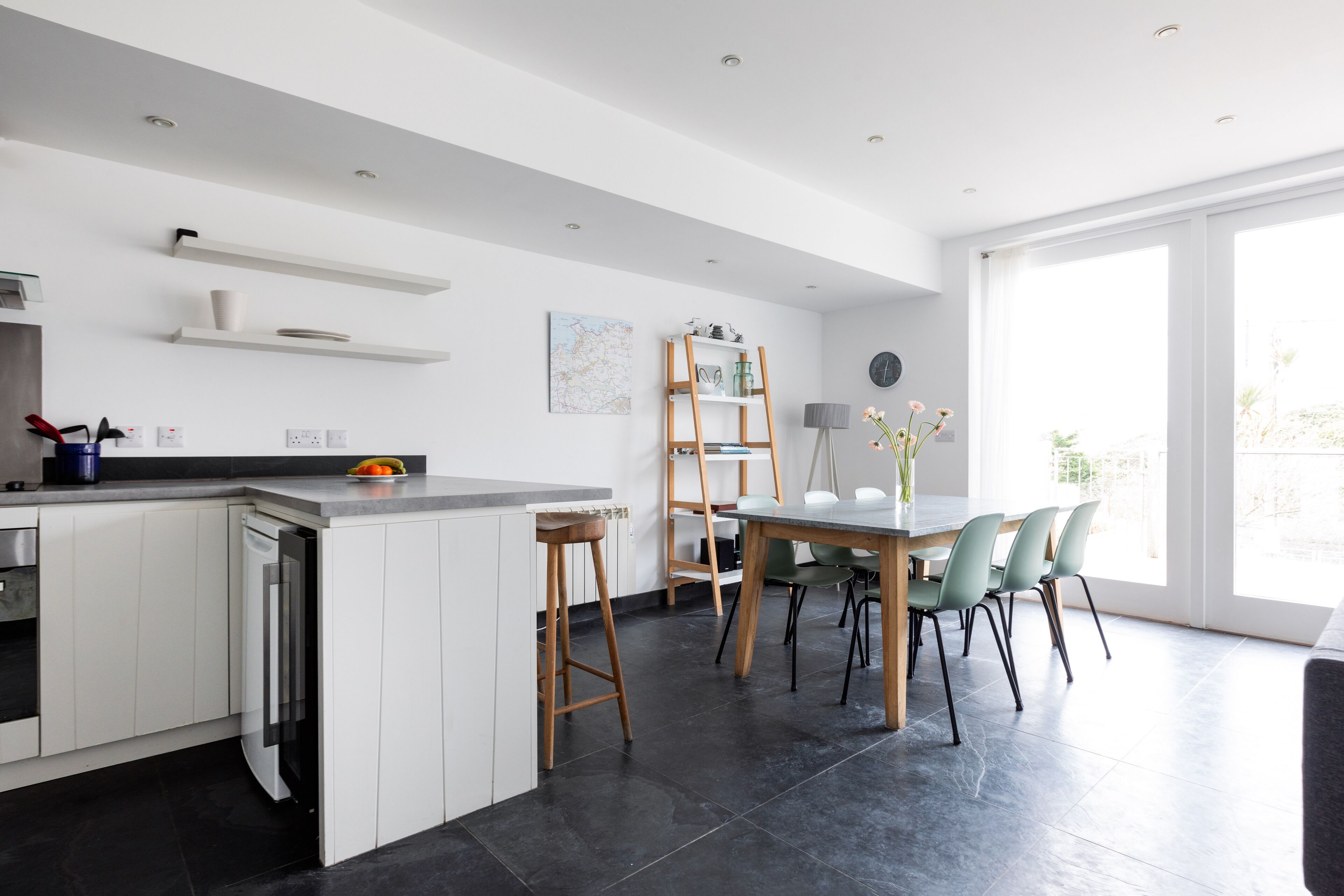 A modern kitchen with white cabinetry, a built-in dishwasher, and a dining area with a wooden table and chairs.