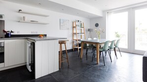 Une cuisine moderne avec des meubles blancs, un lave-vaisselle encastré et un coin repas comprenant une table et des chaises en bois.