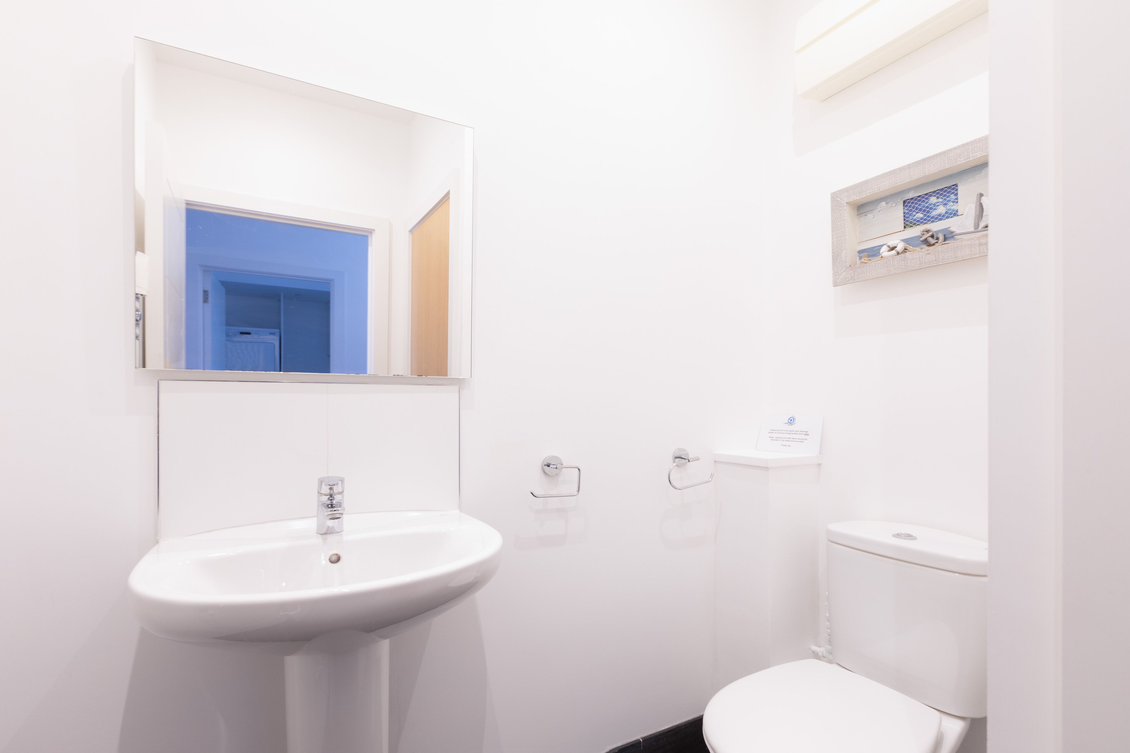 Un baño con lavamanos, inodoro y espejo blancos.