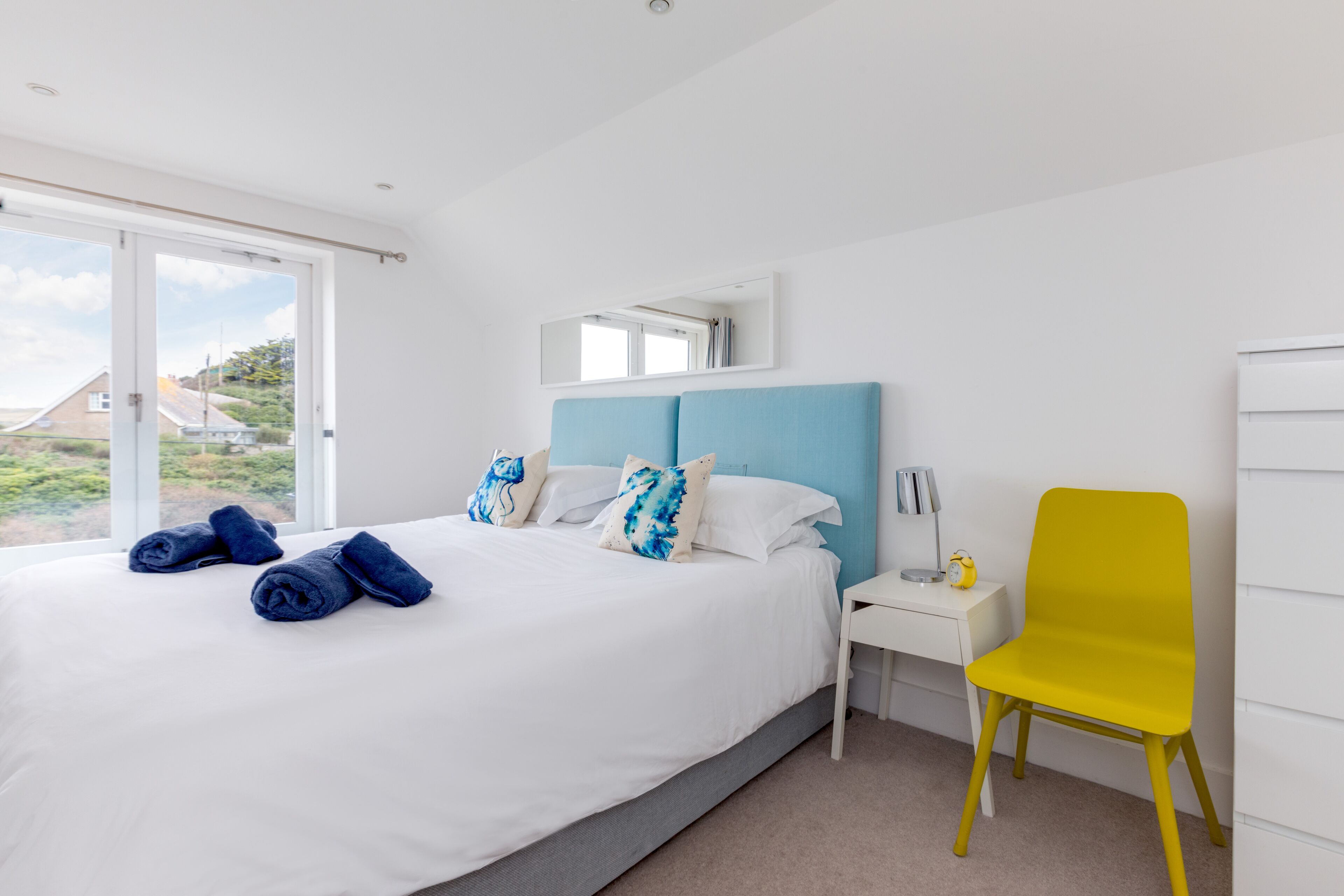 A bedroom with a bed, a nightstand, a chair, and a window with a view.