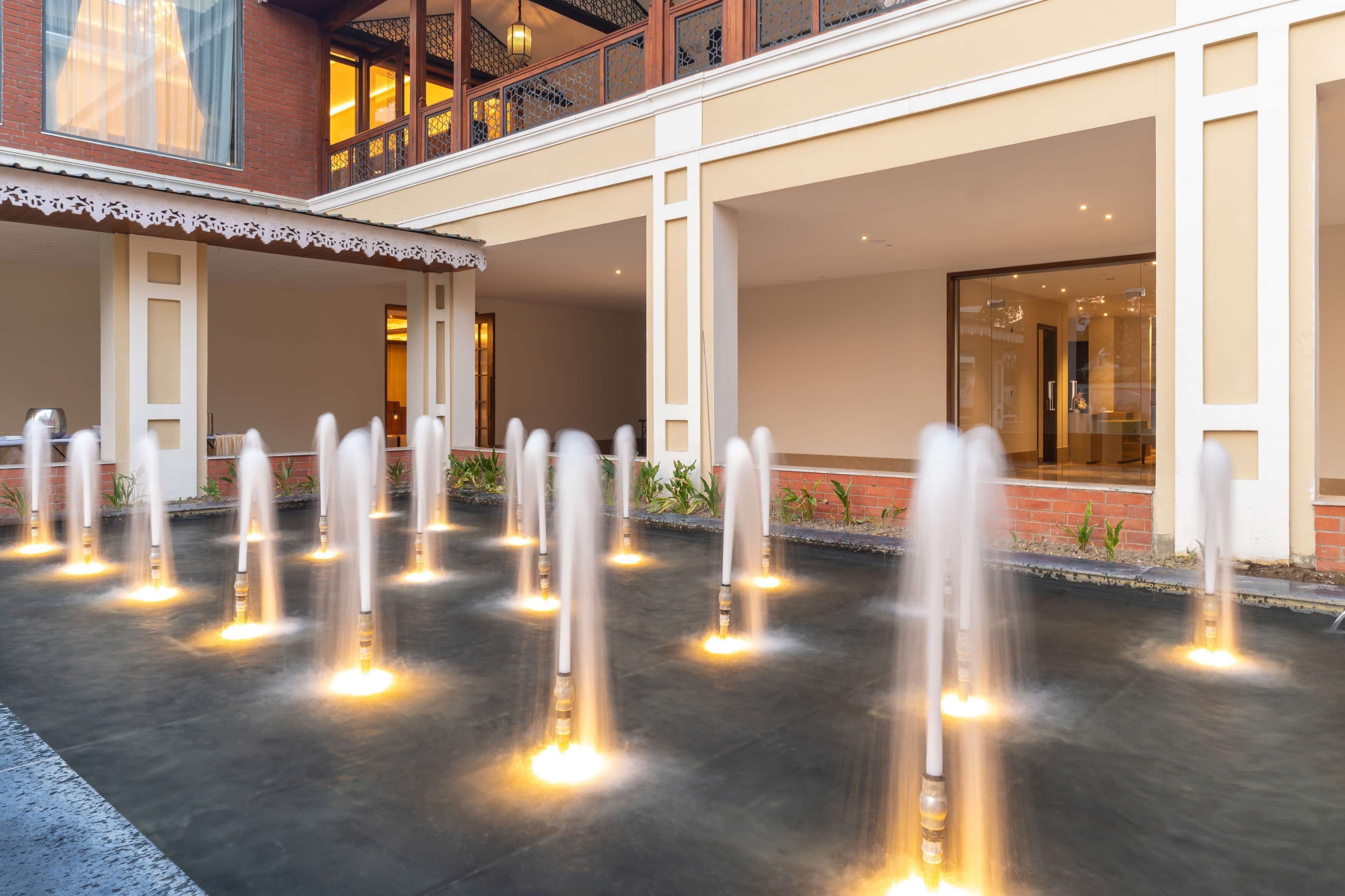 A courtyard with multiple water fountains and a building with a balcony.