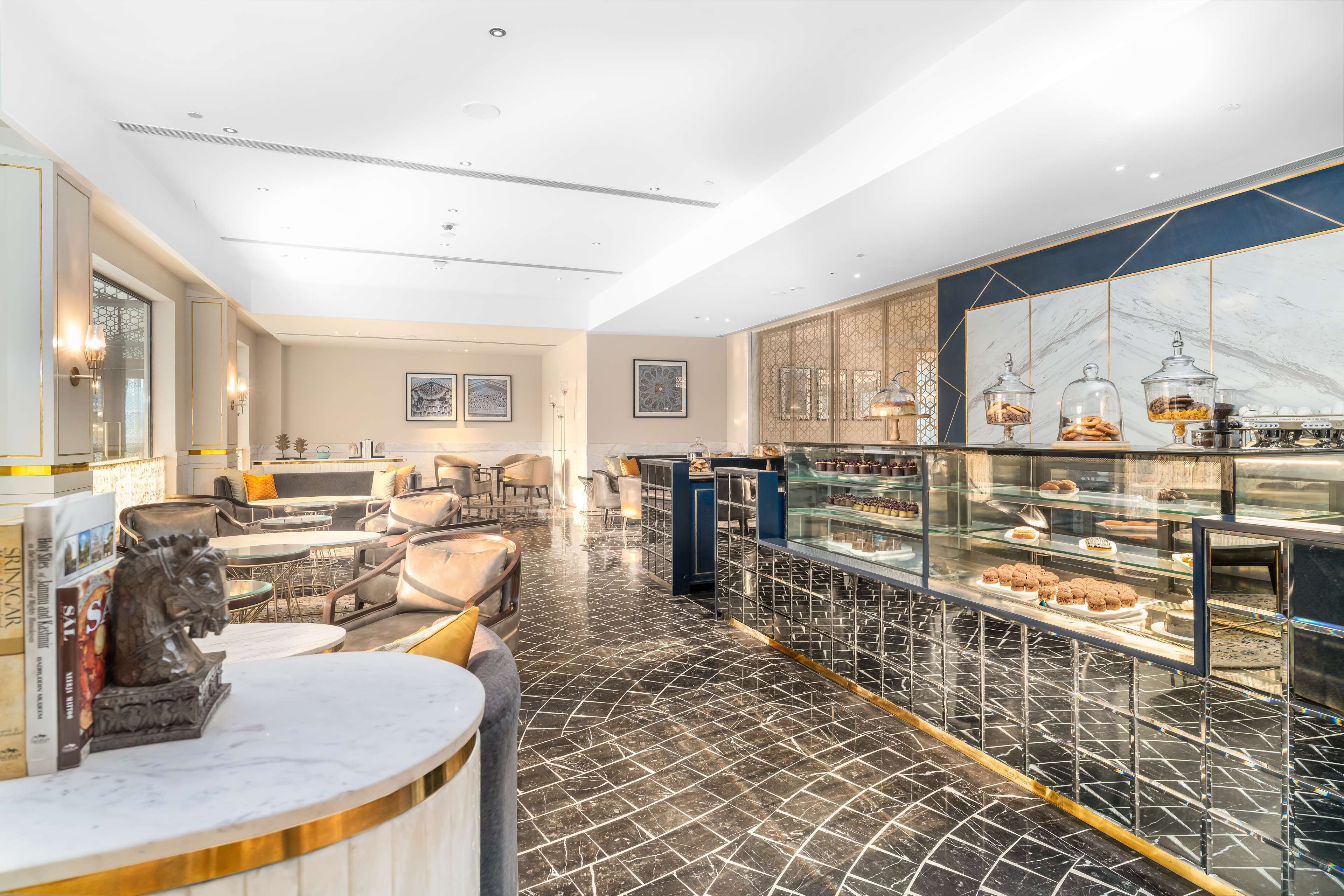 A modern interior with a marble floor, a seating area with sofas and tables, and a bakery display with pastries.