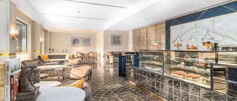 A modern interior with a marble floor, a seating area with sofas and tables, and a bakery display with pastries.