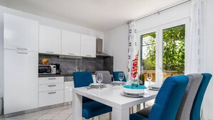 Una cocina moderna con armarios blancos, una mesa de comedor lista para cuatro personas y vistas a zonas verdes por la ventana.