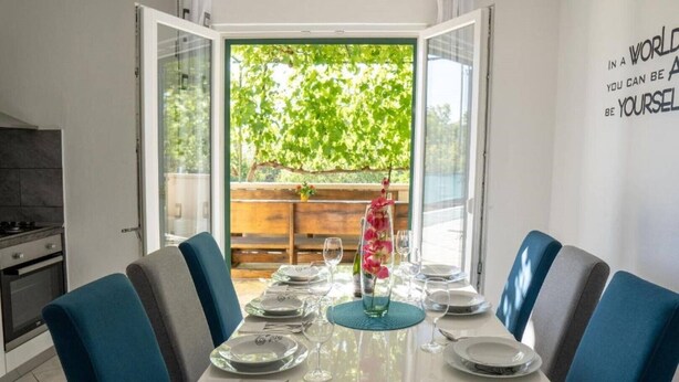 Comedor con una mesa lista para cuatro, cocina al fondo y vista a la vegetación a través de puertas abiertas.