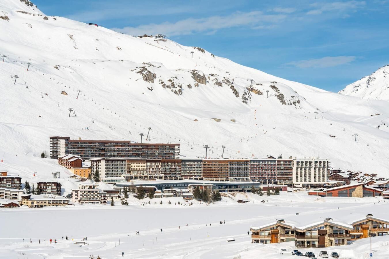 A snow-covered mountain town with a large hotel complex, ski slopes, and a clear sky.