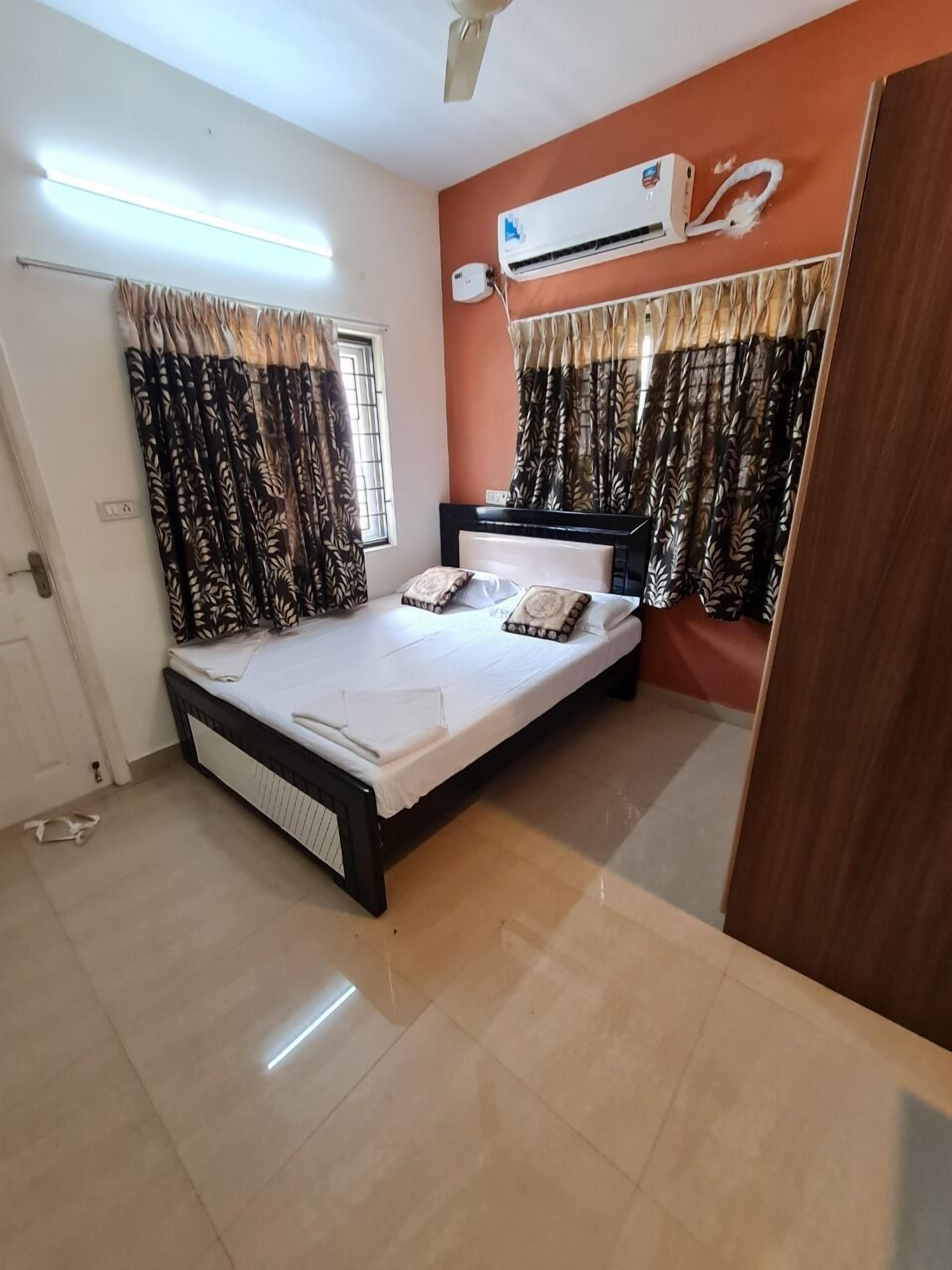 A bedroom with a bed, curtains, an air conditioning unit, and a door.