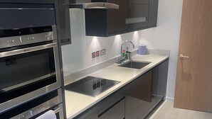 A modern kitchen with stainless steel appliances, a double sink, and wooden cabinets. - Impeccable 2 Bed 2 Bath Penthouse (London)