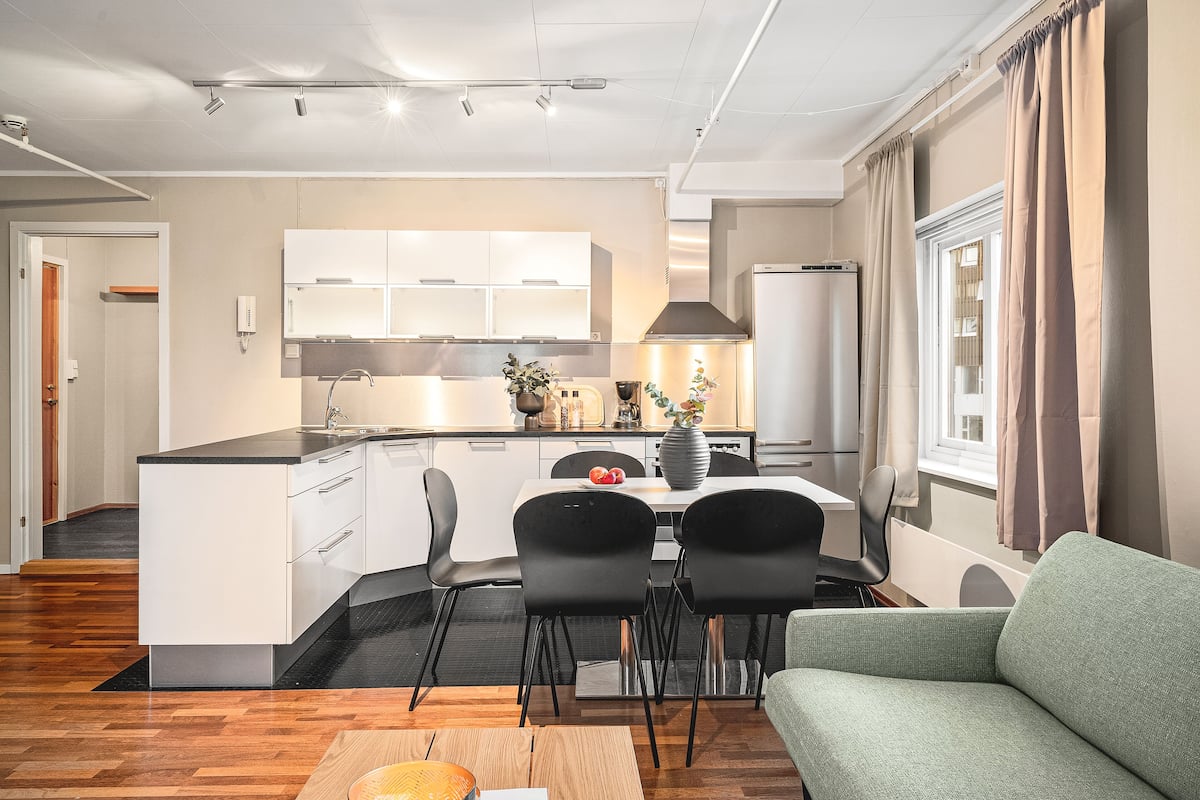 A modern kitchen with white cabinets, a black countertop, and a dining area with two black chairs and a table.