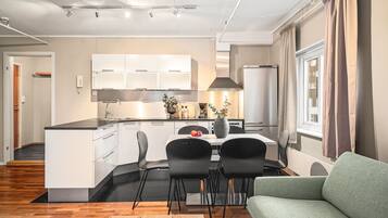 Een moderne keuken met witte kasten, een zwart aanrechtblad en een eethoek met twee zwarte stoelen en een tafel.