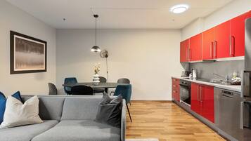 A modern kitchen with red cabinets, a grey sofa, and a dining area with a table and chairs.