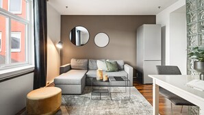 A modern living room with a grey sectional sofa, a round ottoman, a coffee table, and a white desk with a chair. - Amalie Apartments By First (Tromsø)