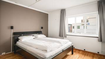 Ein modernes Schlafzimmer mit einem Bett, Nachttischen, einem Fenster mit Vorhängen und Blick auf Gebäude.