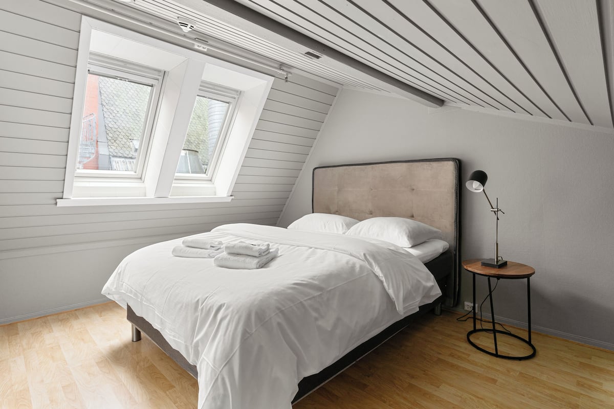 A bedroom with a bed, a bedside table with a lamp, and a window.