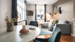 A modern living room with a dining table, chairs, a sofa, and a TV mounted on the wall. - Amalie Apartments By First (Tromsø)