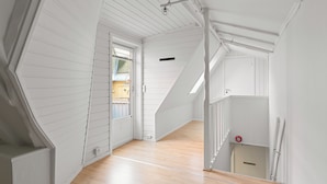 A spacious, white interior with wooden flooring, a staircase, and a door leading to an outdoor area. - Amalie Apartments By First (Tromsø)