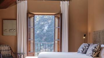 A bedroom with a large window, a bed, a chair, and a painting on the wall.