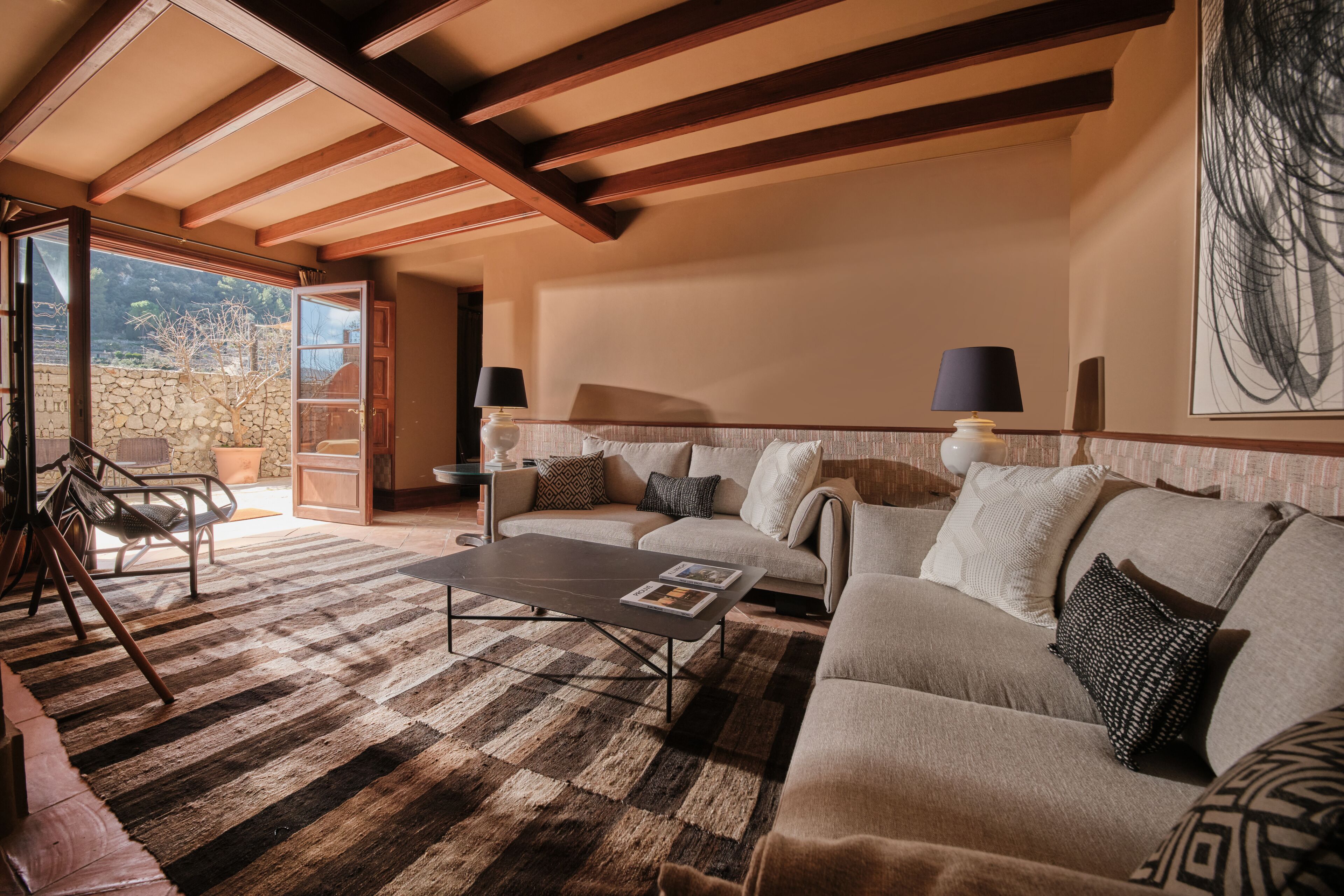 Un salón acogedor con sofá, mesa de centro y sillas. Se aprecia una pared de piedra y un ventanal amplio.