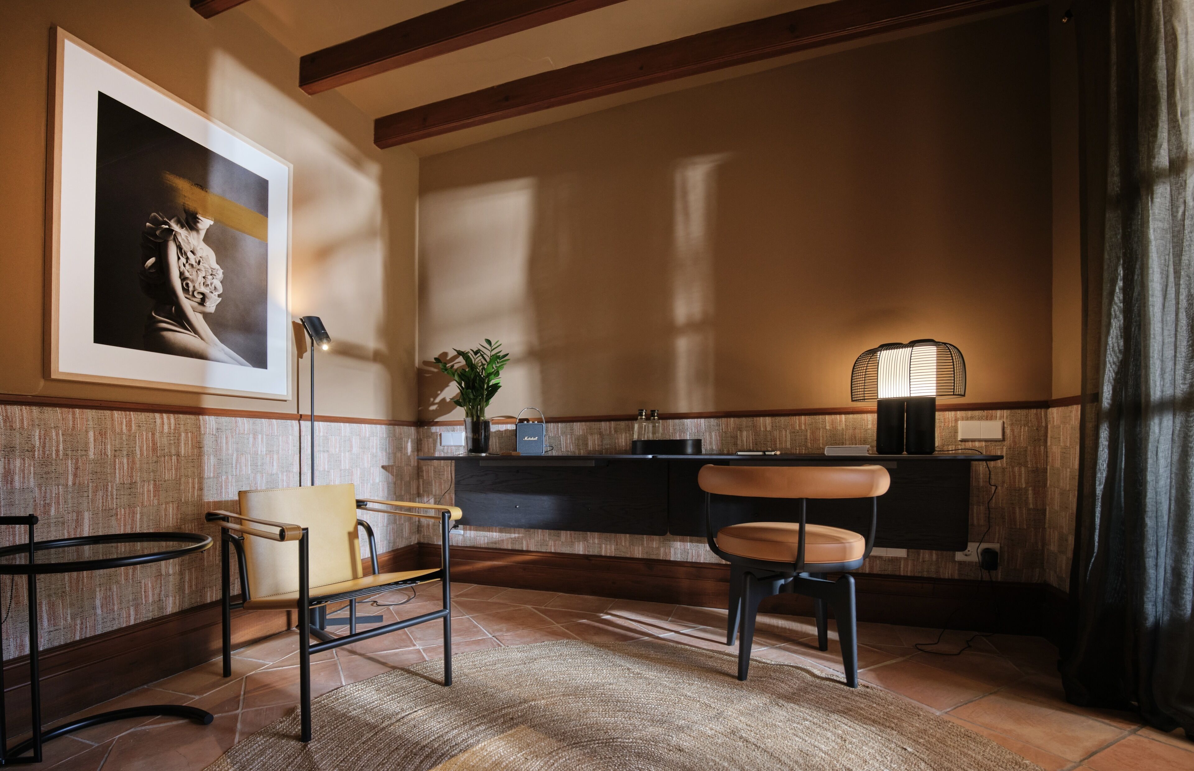 A modern interior with a wooden ceiling, a framed artwork on the wall, a small table with a plant, and two chairs.