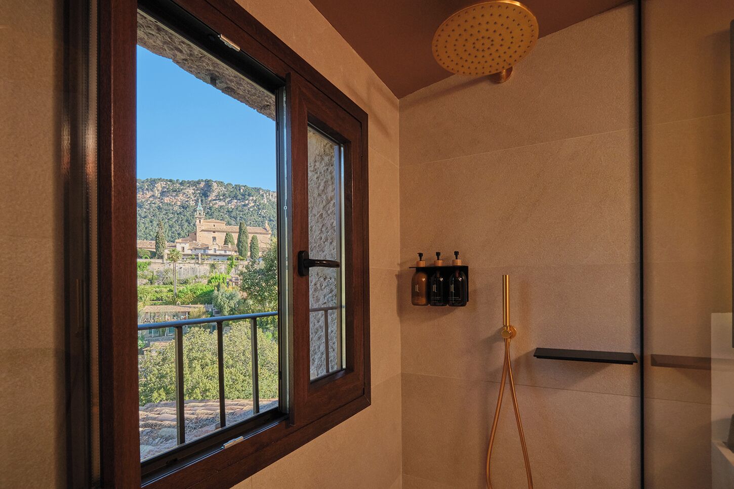 A bathroom with a large window, a shower, and toiletries on a shelf.