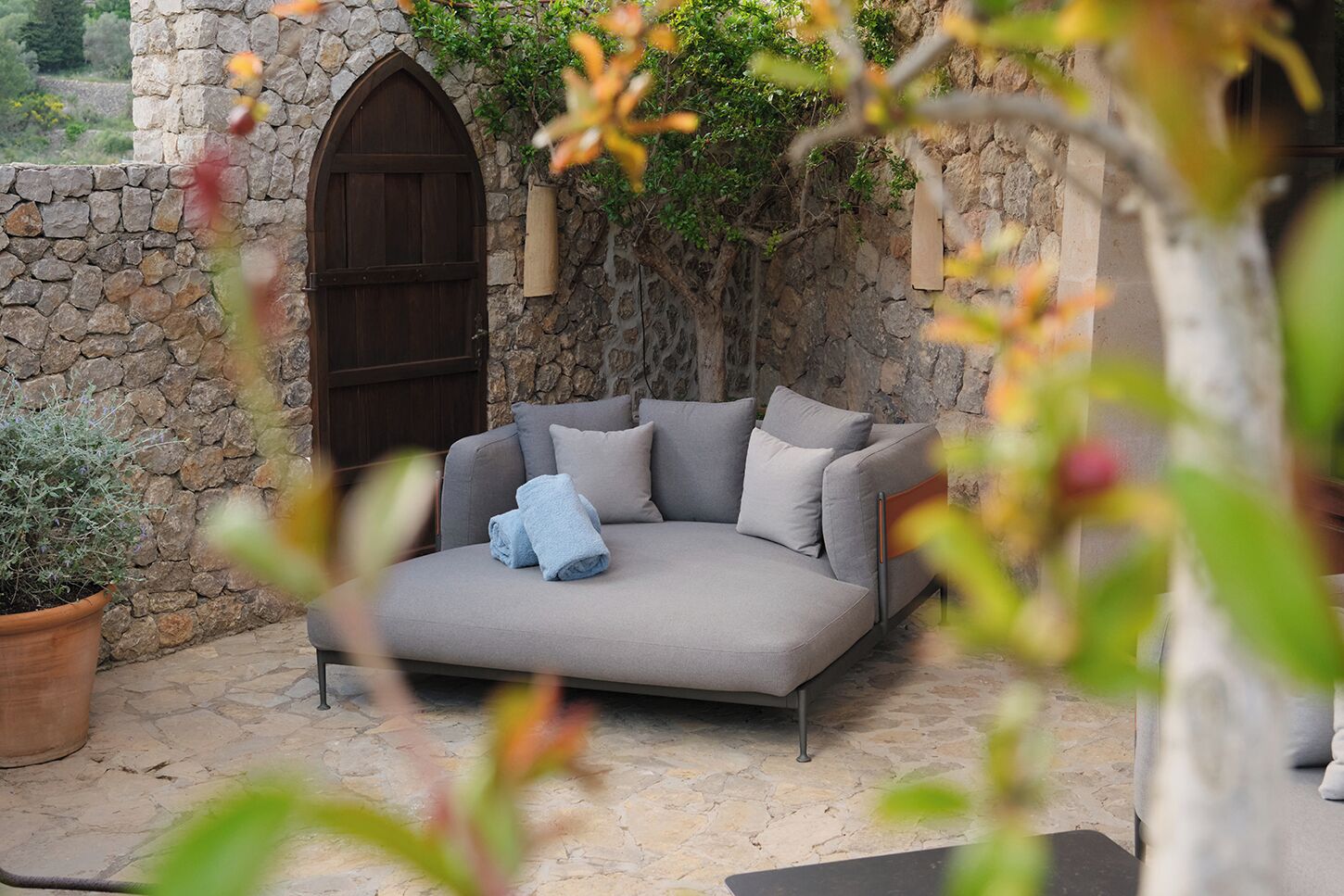 A stone wall with a wooden door, a grey sofa with cushions, and a potted plant.