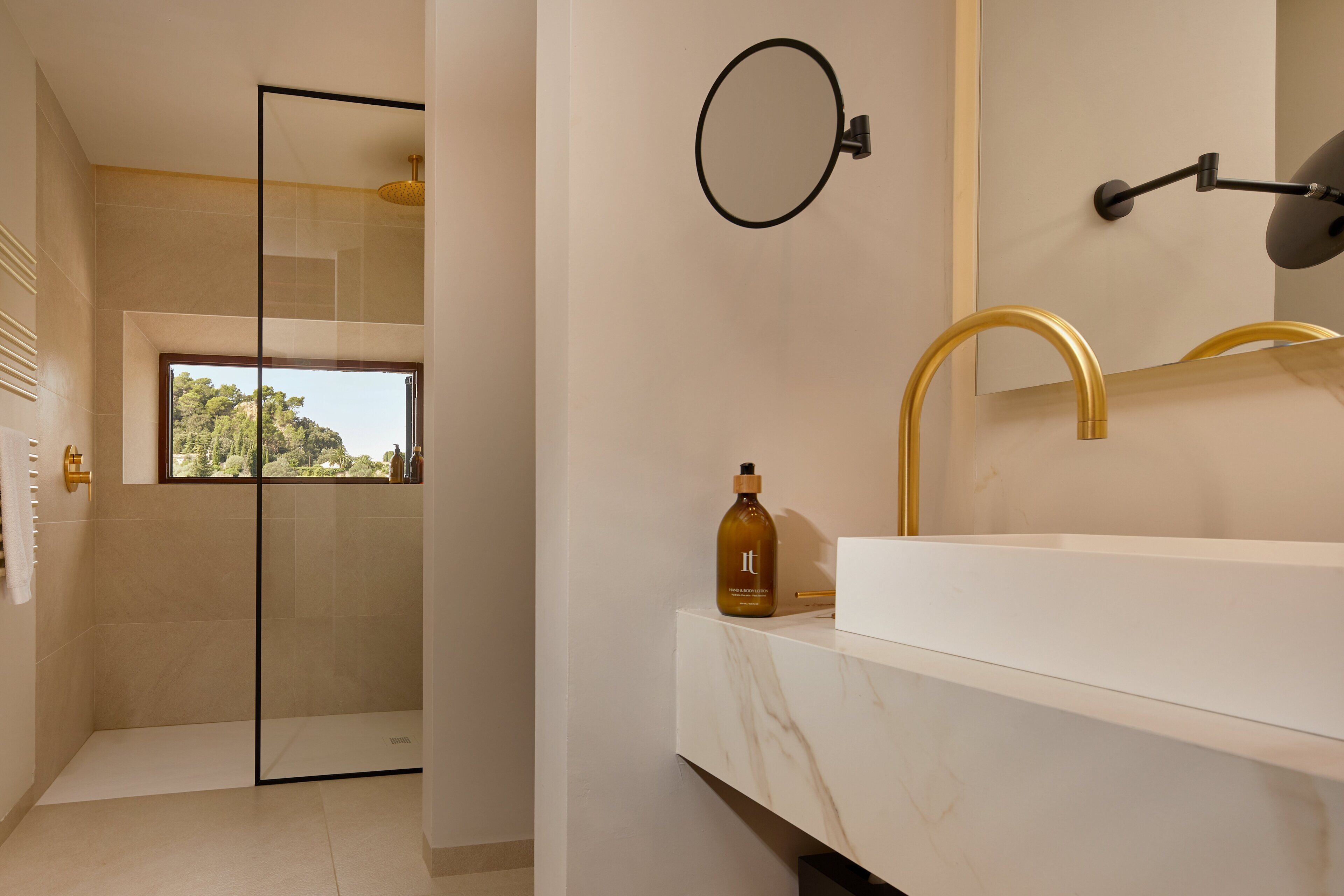 A modern bathroom with a large mirror, gold faucet, and a bottle of shampoo on the counter.