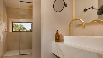 A modern bathroom with a large mirror, gold faucet, and a bottle of shampoo on the counter.