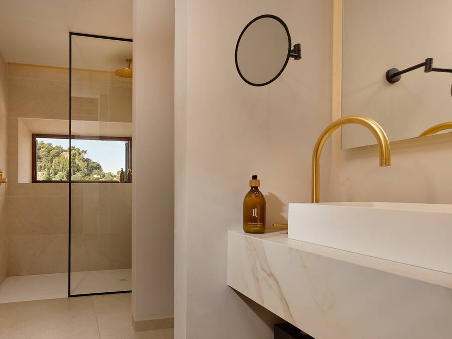 A modern bathroom with a large mirror, gold faucet, and a bottle of shampoo on the counter.