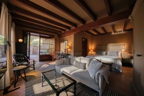 A cozy room with a sofa, a small table, and a bed with two pillows. There is a window with curtains and a door leading outside.