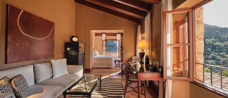 A spacious living area with a sofa, coffee table, and a view of a bedroom through an open doorway.