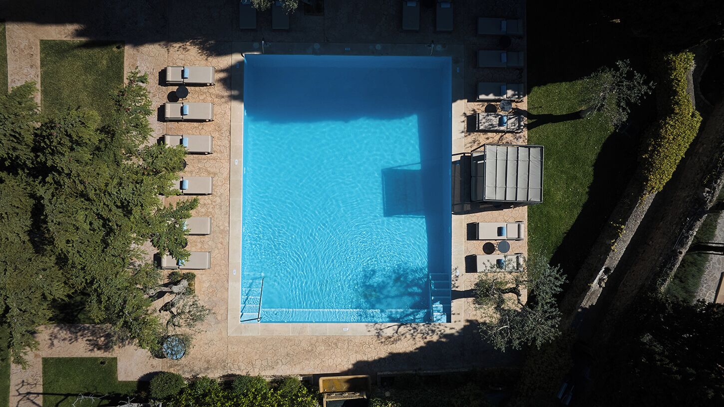 An aerial view of a rectangular swimming pool surrounded by lounge chairs and a small deck area.