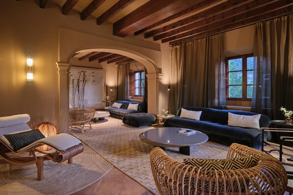 A spacious living area with a dark blue sofa, a round coffee table, and wicker furniture. An arched doorway leads to another room with a large window.