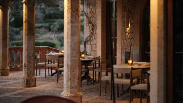 Un área de comedor al aire libre con columnas de piedra, mesas y sillas.