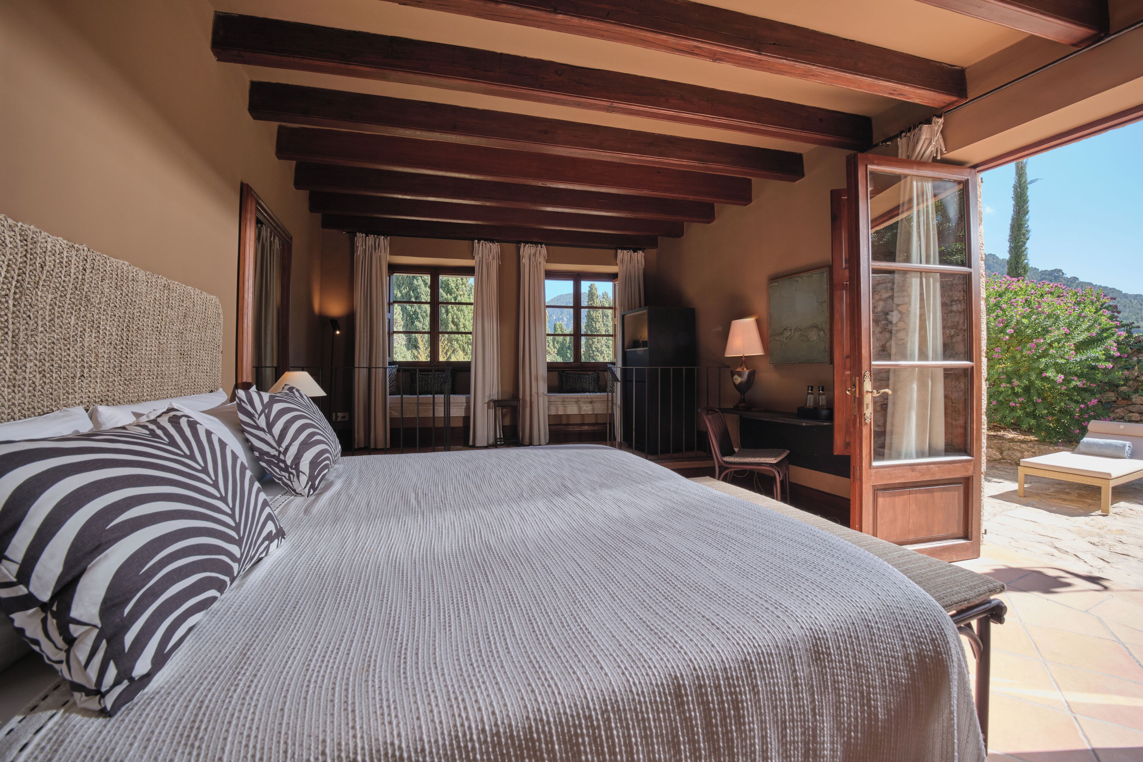 Un dormitorio con una cama grande, un televisor y un escritorio con lámpara. Hay una puerta que da a un espacio exterior con una silla y una mesa.