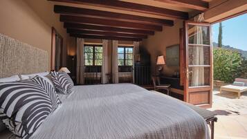 Un dormitorio con una cama grande, un televisor y un escritorio con lámpara. Hay una puerta que da a un espacio exterior con una silla y una mesa.