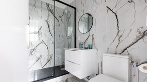 A bathroom with a glass shower enclosure, a white vanity with a mirror, and a toilet. - Home Voltaire (Paris)
