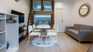 A compact room with a bed, a dining table with chairs, a sofa, a TV, and a mirror. - Home Voltaire (Paris)