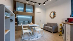 A compact living space with a bunk bed, a dining area with a table and chairs, a sofa, a washing machine, and a mirror on the wall. - Home Voltaire (Paris)