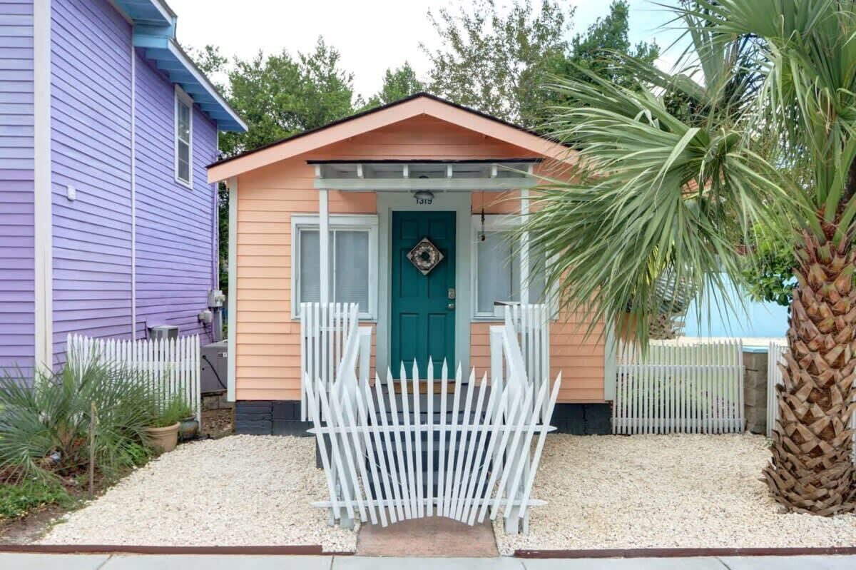 A small house with a teal door, white picket fence, and a palm tree.
