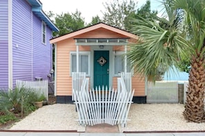 A small house with a teal door, white picket fence, and a palm tree.