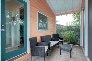 A covered patio area with wicker furniture and a glass door leading to a room.