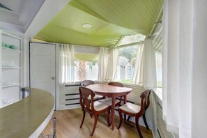 A dining area with a round table and four chairs, a white door, and a window with curtains.