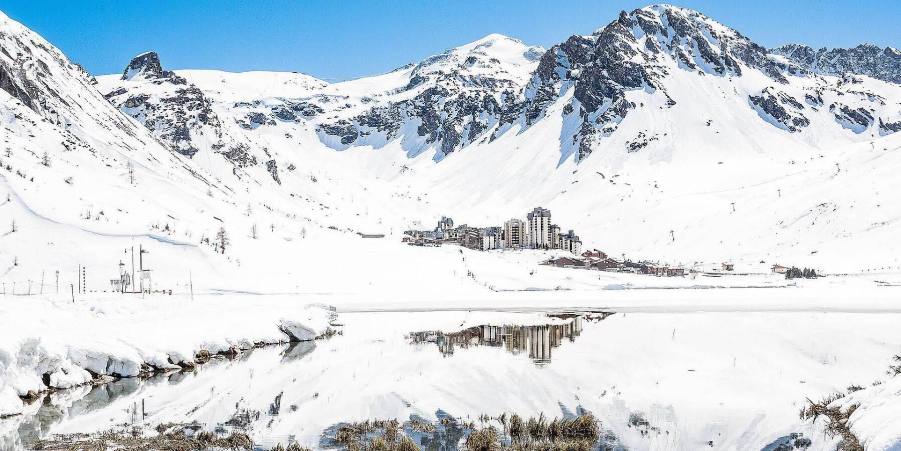 Paisaje montañoso cubierto de nieve con un pueblo pequeño y edificios cerca de un lago.