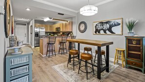 Una cocina moderna con armarios de madera, una isla central con taburetes, una mesa de comedor y una zona de bar.