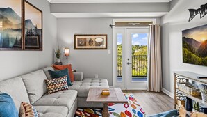 Un salón con un sofá gris, cojines coloridos, una mesa de centro de madera y vistas a un balcón con una puerta que dice "Family Love".