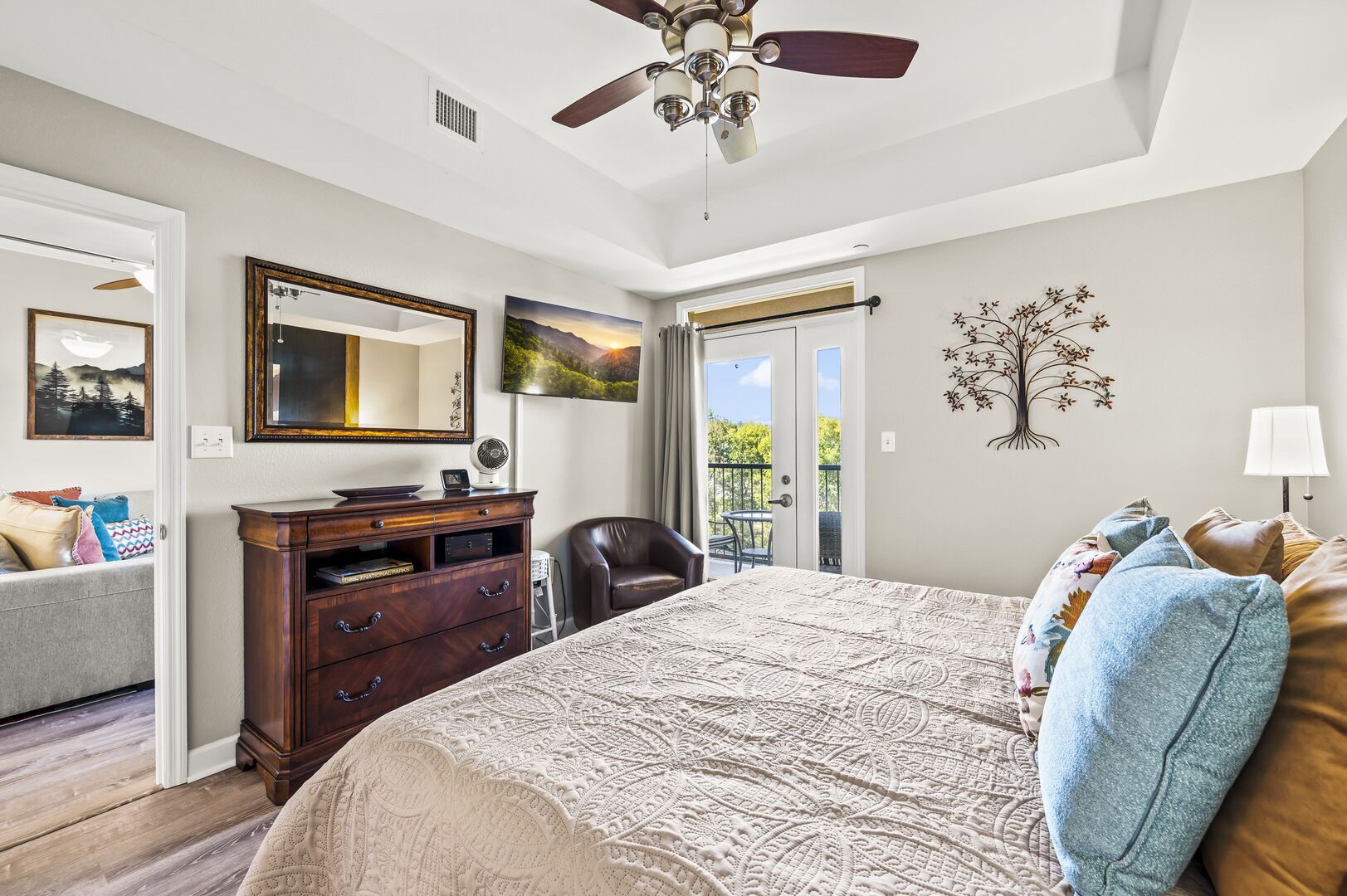 Une chambre avec un grand lit, une commode, une chaise, un ventilateur de plafond, un miroir et un balcon avec vue.