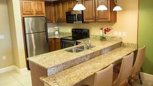 A kitchen with granite countertops, stainless steel appliances, wooden cabinets, and wicker chairs. - Escape to Our Resort in Orlando,s Entertainment Hub Near Theme Parks & Shopping! (Orlando)