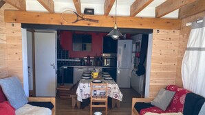 A cozy cabin interior with a wooden dining table, two sofas, a coffee table, and a kitchen in the background.