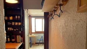 Un pasillo estrecho con un estante de madera a la izquierda, una lámpara colgante y una pared de madera con ganchos.
