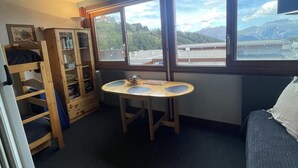 Habitación pequeña con literas, una mesita con un cuenco, y ventana con vistas a la montaña.